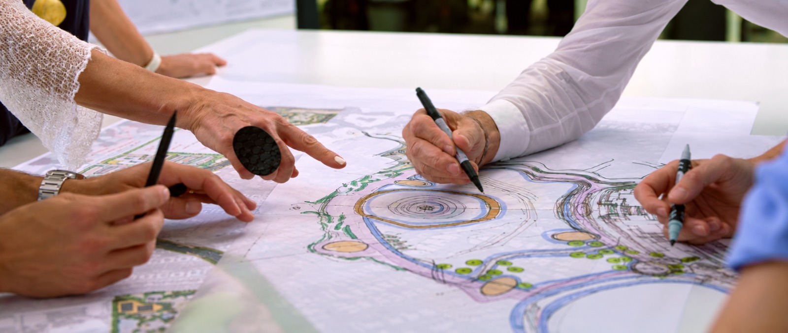 Progettazione del giardino: planimetrie e scelte botaniche al tavolo di lavoro Progettisti al tavolo da disegno con planimetrie a colori di un parco e di un giardino